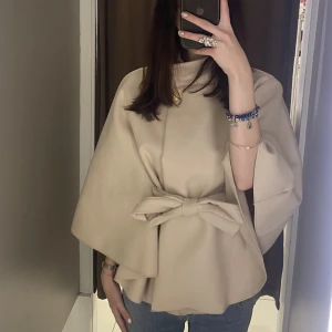 Beige poncho jacka  - Superfin beige kappa från Missäy med breda ärmar och snygg rosett i midjan. Jackan har en elegant och avslappnad passform, perfekt för dig som gillar stilrena och våriga plagg. Materialet känns mjukt och lyxigt, och färgen är lätt att matcha med allt.