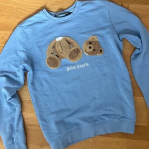 Blå Palm Angels sweatshirt med nalle - Säljer en ljusblå sweatshirt från Palm Angels med ikoniskt nallebroderi på bröstet och vit logga under. 🧸orginalpris är ungefär 4000kr. 🩵 (är inte helt hundra om den är äkta) 