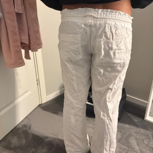 Vita linnebyxor med snörning - Säljer ett par vita linnebyxor med bred resår i midjan och snörning framtill. Byxorna har raka ben och stora fickor både fram och bak. Perfekta för chill dagar eller när du vill ha en luftig och skön stil som när de är varmt ute t.ex. Ej strukna på bilden men stryks om det skulle viljas innan frakt