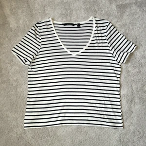 Randig v-ringad t-shirt - Vit t-shirt med svarta horisontella ränder från Vero Moda. T-shirten har v-ringning, är kroppad och har korta ärmar, perfekt för en avslappnad och stilren look. 