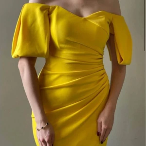 Gul offshoulder klänning med puffärm - Snygg gul klänning med offshoulder och puffiga korta ärmar. Omlott-detalj framtill och drapering i midjan ger en riktigt trendig siluett. Perfekt för dig som vill sticka ut med färg och stil. Klänningen har en kort längd och markerad midja. Klänningen är köpt från Asos och endast använd en gång