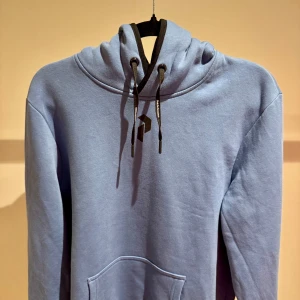Ljusblå hoodie från Peak Performance - Säljer en ljusblå hoodie från Peak Performance med svart logga på bröstet och ryggen. 