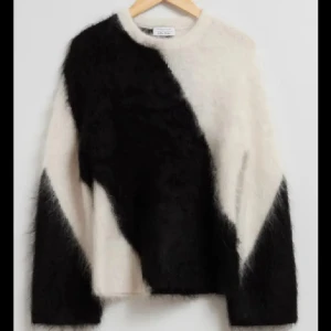 Svartvit fluffig stickad tröja - Supermjuk och fluffig stickad tröja från & other stories i svart och vitt. Tröjan har ett coolt, asymmetriskt mönster och är långärmad med relaxed fit. Perfekt för dig som gillar statement-plagg med skön känsla.