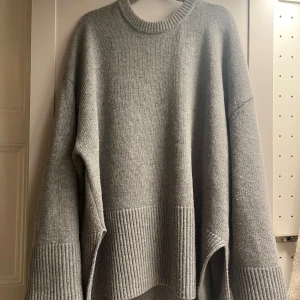 Stickad tröja - Säljer en mjuk grå stickad tröja från H&M i ull- och kashmirblandning. Tröjan har oversized passform, rund halsringning och breda ribbade muddar vid ärmslut och nederkant.