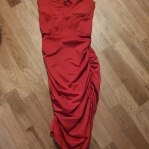 Röd långklänning från Nelly - Snygg röd långklänning från Nelly med smala axelband och figurnära passform. Klänningen har rynkade detaljer längs ena sidan och markerad byst. Perfekt för dig som vill sticka ut med en elegant och trendig look.