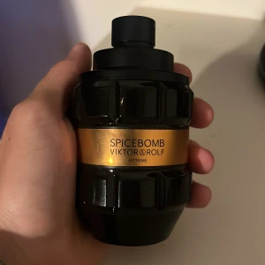 Spicebomb Extreme från Viktor & Rolf - Kraftfull parfym i svart, robust flaska med guldigt band och texten 'Spicebomb Extreme'. Flaskan har en unik, granatinspirerad form och känns lyxig och maskulin. Perfekt för dig som gillar kryddiga och intensiva dofter.
