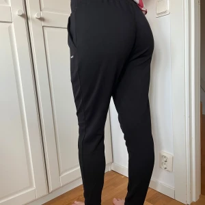 Svarta mjukisbyxor med snörning - Svarta mjukisbyxor med dragsko i midjan och fickor på sidorna. Byxorna har en slim passform och är tillverkade i mjukt bomullsmaterial. Perfekta för chill dagar eller när du vill vara bekväm men ändå se fräsch ut.