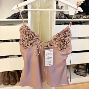 Zara topp champagne - Champagne / brons färgad topp från Zara med blom detaljer över bröstet, super fin helt oanvänd. Banden får att spänna åt själv. Lappen kvar. 