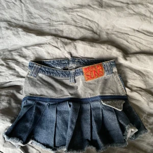 Jeanskjol Replay Sins med patch och volang - Unik kort jeanskjol från Replay med coolt 'SINS'-patch fram och volang nedtill. Kjolen har flera denimnyanser, dekorativa fickor och bandanamönster baktill. Perfekt för dig som vill sticka ut med en edgy och kreativ stil.