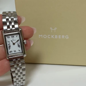 Mockberg silverfärgad rektangulär klocka - Stilren klocka från Mockberg med rektangulärt ur i silverfärg och vit urtavla med romerska siffror. Länken är i blankt metall och ger en klassisk vibe. Perfekt accessoar för dig som gillar tidlös design och snygga detaljer. Aldrig använt 