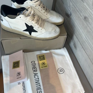 Golden Goose Ballstar - Golden Goose sneakers i vitt skinn med svart stjärna på sidan och svarta detaljer vid häl och plös. Beige snörning och vintage-inspirerad, något smutsad sula. Klassisk rund tå och platt sula. Perfekta för dig som gillar en cool och avslappnad stil. Helt nya.