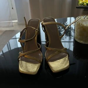 Guldiga sandal klackskor - Strappy sandaler i metallic guld med fyrkantig tå och bred blockklack. Köpte från Zara, använd 1 gång på bröllop men köpte fel storlek 