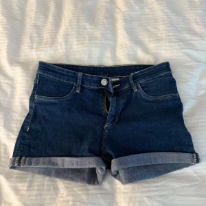 Mörkblå jeansshorts från &Denim - Snygga mörkblå jeansshorts från &Denim med klassisk femficksdesign och uppvikta benslut. Shortsen har normal passform och lågmidja, perfekta för sommardagar. Gjorda i mjukt denimtyg med dragkedja och knapp framtill. Det är storlek 158 men passar storlek xs/s.