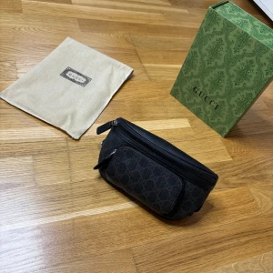 Svart Gucci axelväska med GG-mönster - Snygg svart axelväska från Gucci med klassiskt GG-mönster. Väskan har flera fack med dragkedja och justerbart band med spänne. Tillverkad i skinn och polyester, perfekt för att bära det viktigaste. Kommer med originalpåse och grön Gucci-box.