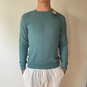 Turkos kabelstickad tröja Stenströms - Kabelstickad turkos tröja från Stenströms i mjuk merinoull. Tröjan har rund halsringning, ribbade muddar och lång ärm. Perfekt för dig som gillar klassisk stil med modern touch. Den är ganska tunn och perfekt till sommaren. Modellen på bilden är 188 och väger ca 85kg och den är lite för tight för han!