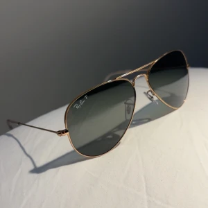 Ray-Ban Aviator  - Snygga Ray-Ban Aviator solglasögon med tunna guldfärgade metallbågar och mörka, polariserade linser. Klassisk pilotform som ger en tidlös vibe. Perfekta för att lyfta din stil under soliga dagar. Priset kan diskuteras!😁
