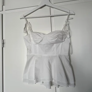 Vit korsettopp från Zara med knyt - Supersöt vit korsettopp från Zara med tunna axelband som knyts på axlarna. Toppen har markerade kupor, figurnära passform upptill och en lätt utsvängd, volangig nederdel. Perfekt för sommarens alla tillfällen och ger en romantisk vibe. ANVÄND 1 GÅNG OCH VÄLDIGT BRA SKICK!