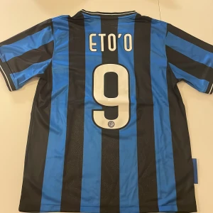 Inter Milan Eto'o 9 Finaltröja Nike - Inter Milan fotbollströja replika med Eto'o och nummer 9 på ryggen. Officiell Champions League-final 2010-version med Pirelli-tryck, klubbmärke och Nike-logga. Svart och blå vertikala ränder, kortärmad och tillverkad i lätt funktionsmaterial. Endast handtvätt!
