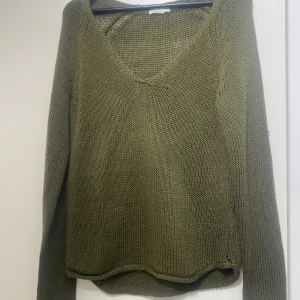 Olivgrön stickad tröja från H&M - Olivgrön stickad tröja från H&M med v-ringning och lång ärm. Tröjan har en avslappnad passform och är tillverkad i ett grovstickat material som känns både chill och snyggt. Perfekt att slänga på sig över ett linne eller t-shirt.