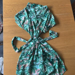 Palmmönstrad kortklänning från Monki - Superfin kortklänning från Monki med tropiskt palmmönster i grönt, blått och rosa. Omlottmodell med knyt i midjan❣️❣️ Strl S!!❣️❣️