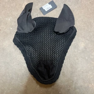 Svart ridhuva med öron - Klassisk design med diskret kant och helsvart look. Passar till ridning och tävling. Aldrig använd, ny med prislapp.