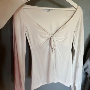 Vit långärmad topp med knyt - Superfin vit långärmad topp från Design by Si. Djup v-ringning och snygg knytdetalj framtill som ger en tusch. Perfekt att styla med jeans eller kjol för en clean look. Den passar mig som brukar oftast använda storlek xs/s! Den är lite beige då det blivit så i tvätten men ändå vit.
