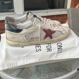 Golden Goose sneakers med röd stjärna - Snygga sneakers från Golden Goose i vitt skinn och mesh med svart hälkappa och ikonisk röd stjärna på sidan. Dust bags tillkommer också samt box. Lite defekter på bakre häl men inget som syns om man inte kollar nära, och påverkar inte helhetsintrycket! Kvitto finns så hör av er för mer info och bilder!