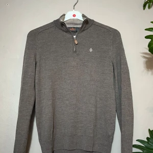 Grå merinoulltröja från Morris - Snygg grå långärmad tröja från Morris i 100% merinoull. Tröjan har half zip med läderdetalj, broderad logga på bröstet och ribbade muddar. Perfekt för dig som gillar stilren och klassisk look med en modern touch. OBS DEN ÄR GANSKA LITEN I STORLEK!!!