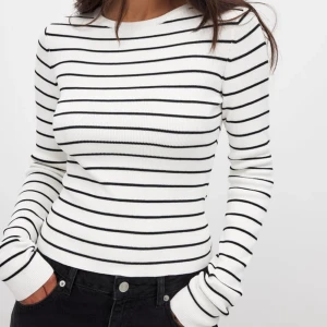 Randig ribbad tröja från  - Säljer en vit långärmad tröja från NA-KD med svarta horisontella ränder. Tröjan är ribbad och har en tight passform med rund halsringning. Perfekt att styla med jeans eller kjol för en clean och fräsch look.