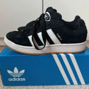 Adidas Campus svarta sneakers💖 - Svarta Adidas Campus sneakers med klassiska vita ränder och vit sula. Skorna har rund tå, snörning och är tillverkade i mocka med detaljer i syntet. Perfekta för en clean streetstyle-look.