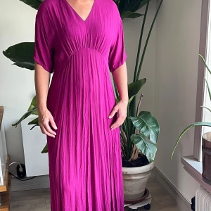 Lång cerise klänning Bitte Kai Rand - Säljer en lång, cerise klänning från Bitte Kai Rand med v-ringning och korta ärmar. Använd 1 gång. Klänningen har ett snyggt rynkat parti under bysten och är tillverkad i ett lätt, skrynkelfritt tyg som faller fint. 