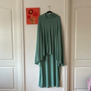 Ljusgrön långklänning med matchande khimar  - Säljer en ljusgrön långklänning med matchande khimar. Klänningen har lång ärm, hög krage och är gjord i ett mjukt, stretchigt syntetmaterial (jearsy).  Khimaren ger en extra cool och flytande look. Perfekt för dig som vill sticka ut med en unik och stilren outfit.