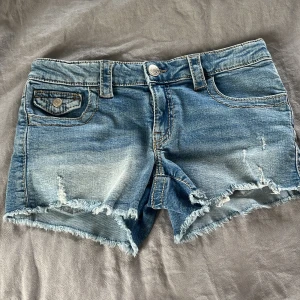 Blå jeansshorts med fransig kant - Snygga blå jeansshorts med slitna detaljer och fransig kant nertill. Klassisk femficksmodell med coola ficklock bak och fram, samt silverfärgade knappar. Perfekta för varma dagar när du vill ha en avslappnad och trendig look. Shortsen är i strl 158 och aldrig andvända. Skriv privat för fler frågor eller bilder💙
