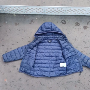 Blå pufferjacka med avtagbar huva - Säljer en blå pufferjacka från OCNWORKS med avtagbar huva och dragkedja framtill. Jackan är quiltad och har långa ärmar. Perfekt för kyliga dagar och enkel att anpassa med huvan som kan tas av med tryckknappar.