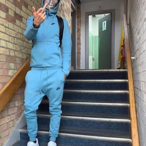 Nike ljusblå mjukisbyxor  - Nike mjukisbyxor i ljusblått med svarta detaljer och logga på låret. Byxorna har snörning i midjan, smal passform och dragkedja på ena benfickan. Perfekta för chill eller träning, tillverkade i mjuk bomullsblandning.