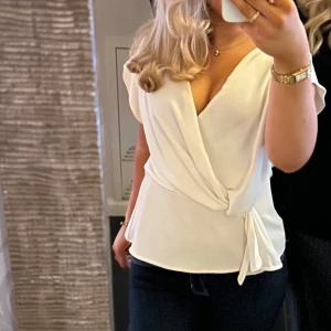 Vit omlottopp från Zara - Säljer en stilren vit omlottopp från Zara med v-ringning och knyt i sidan. Toppen har korta ärmar och en lätt, flowy känsla som ger en snygg siluett. Perfekt att matcha med jeans eller kjol för en fräsch look. Passar till både en sommar och vinteroutfits och sitter så bra!! Perfekt till midsommar. Säljer pågrund av att jag inte använder den längre.♥️