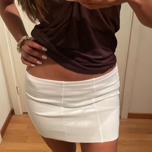 Vit kortkjol i stretchigt tyg - Säljer en vit kortkjol med stilrena sömmar och figurnära passform. Kjolen är enkel och clean i designen, perfekt för dig som gillar minimalistisk stil. Materialet känns stretchigt och bekvämt, vilket gör den lätt att bära hela dagen.