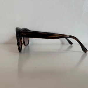 Bruna fyrkantiga solglasögon Fellepini - Snygga solglasögon från Fellepini med brunmelerad, fyrkantig båge och mörka tonade glas. Klassisk och stilren design som ger en cool vibe. Perfekta för att lyfta din look under soliga dagar.