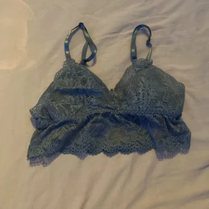 Blå spetsig linnetopp med smala band - Supersöt blå linnetopp i spets med blommigt mönster och smala justerbara axelband. Toppen har v-ringning och fina spetsdetaljer längs kanterna, perfekt för lager-på-lager eller som statement-piece. Mjuk och bekväm känsla tack vare fodrad insida.