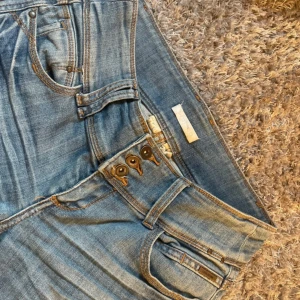 Blå jeans från Promod Love Denim - Snygga blå jeans från Promod Love Denim med raka ben /bootcut och klassisk femficksmodell. Jeansen har låg midja, knäppning med tre synliga knappar och detaljerade sömmar. Midjemått:38 innerbenslängd 84