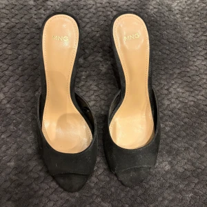 Svarta klackskor från Mango i mocka - Stilrena svarta pumps från Mango i mocka med öppen tå och hög klack. Snygg minimalistisk design med rundad framdel och klassisk siluett. Perfekta för dig som gillar en elegant look med en touch av edge.