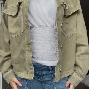 Beige overshirt från Amisu - Snygg grön overshirt från Amisu med guldiga knappar och två stora bröstfickor. Jackan är i bomull och har en rak, lite loose passform. Perfekt att slänga över en t-shirt för en chill och trendig look. Knappast använd!