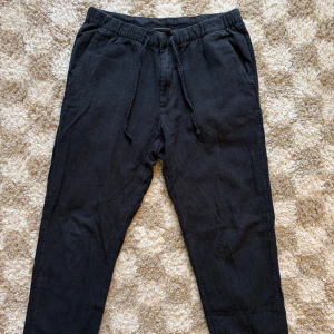 Svarta linnemixbyxor från H&M, strl S - Svarta byxor från H&M i regular fit med snörning i midjan. Tillverkade i en skön linnemix (52% linne, 48% bomull) som ger en avslappnad känsla. Byxorna har sidfickor och en bakficka. Köpte förra sommaren men är väl använda. Något liten i storlek.