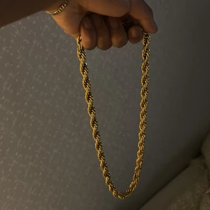 Guldfärgat tvinnat halsband - Säljer ett snyggt cordel halsband i guldfärg med tvinnad kedja som ger en fet och trendig look. Perfekt accessoar för att lyfta din outfit med lite extra bling. Halsbandet har en klassisk karbinhake och känns rejält och stilrent.