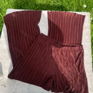 Plisserade vinröda byxor från Zara - Säljer ett par vinröda plisserade byxor från Zara i storlek L. Byxorna har breda ben, elastisk midja och är gjorda i ett glansigt, lätt material som ger en snygg flowy känsla. Perfekta för dig som gillar statement-plagg med cool struktur.