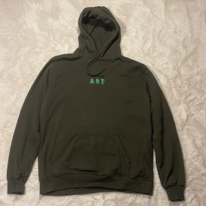 Olivgrön hoodie från Vaillent - Säljer en olivgrön hoodie från Vaillent med broderad text 'ART' i grönt på bröstet. Tröjan har huva med snörning, känguruficka och långa ärmar. Perfekt för dig som gillar en clean och stilren look.