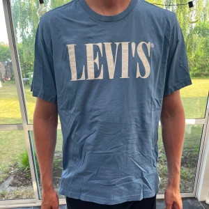 Blå Levi's t-shirt relaxed fit - Snygg blå t-shirt från Levi's med stort vitt logotryck på bröstet. Modellen är relaxed fit och har klassisk rund hals och korta ärmar. Tillverkad i mjuk bomull, perfekt för en chill och stilren look.
