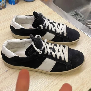 *SÄLLSYNTA* Saint Laurent SL02 sneakers  - Snygga svarta och vita sneakers från Saint Laurent med klassisk låg profil. Skorna har mocka och skinnpaneler, vita snören och en platt sula. Perfekt för dig som gillar stilrena och lyxiga detaljer i vardagen. Skriv om ni har frågor eller funderingar!!! PRIS EJ HUGGET I STEN! Storlek 42 men kan passa 43 