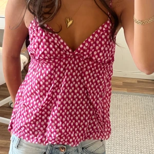 Rosa prickig linnetopp med smala axelband - Supersöt rosa linnetopp med vita prickar och smala axelband. Toppen har v-ringning och lätt rynk under bysten för en avslappnad passform. Perfekt för varma dagar och ger en lekfull vibe till din outfit. Längden har jag klippt själv!