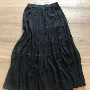 Svart långkjol  - En svart långkjol med avslappnad passform och resår i midjan. Kjolen är sydd i flera våder för en flowy känsla och är gjord i mjuk bomull. Perfekt för dig som gillar en enkel men snygg stil.